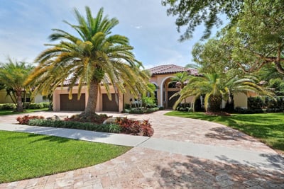 Mediterranean-style home with an arched entry, palm trees, and a curved driveway.