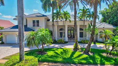 Large stucco home with a tiled roof, central entry, and palm trees across the front lawn.