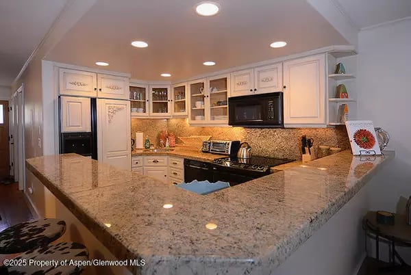 Kitchen with a wide granite peninsula, light wood cabinetry, and built-in appliances.