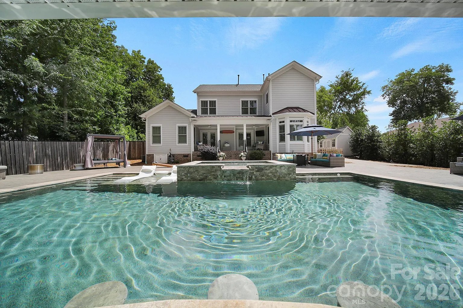 White two-story house behind a turquoise pool with a raised stone spa and waterfall.