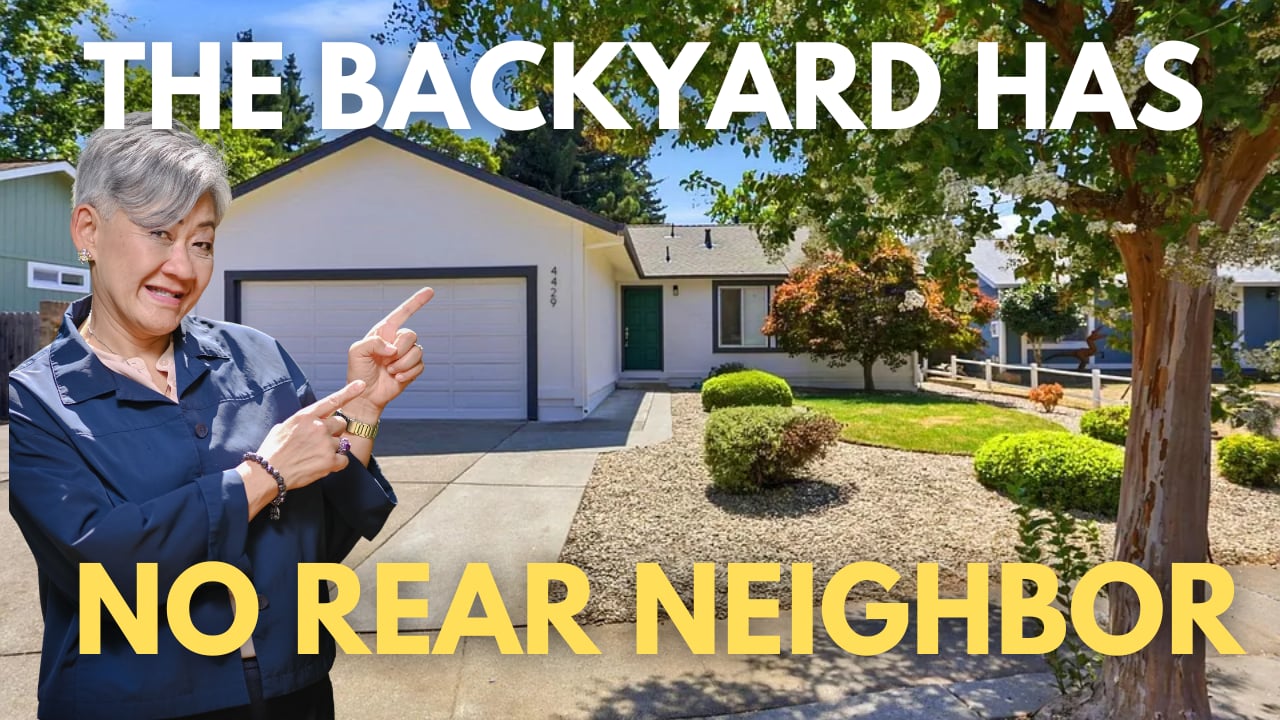 Single-story home with an attached garage and landscaped yard; a woman points toward the house.