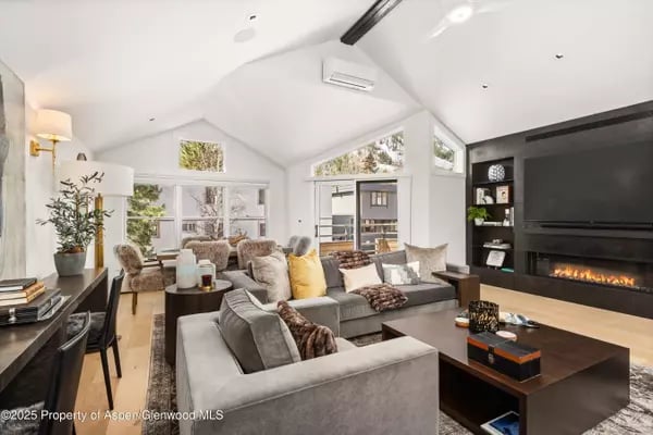 Vaulted living room with gray sofas, large windows, and a built-in fireplace.