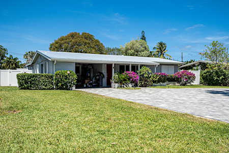 Single-story home with a broad lawn, paved driveway, and flowering tropical shrubs.