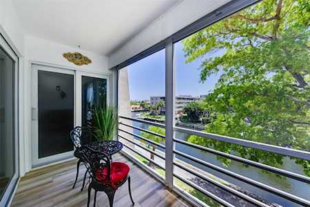 Apartment balcony with black chairs and red cushions overlooking a waterway and leafy tree.