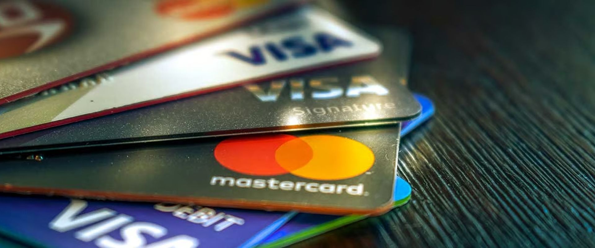 Overlapping Visa and Mastercard payment cards on a dark wooden surface.