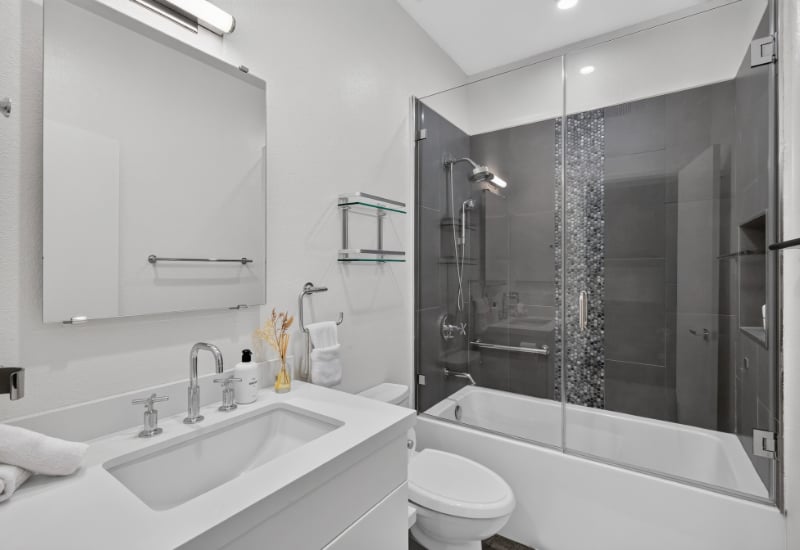 Modern bathroom with a white vanity and a glass-enclosed tub and shower against dark gray tile.