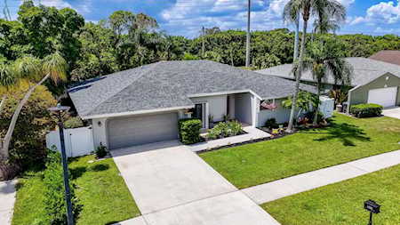 Single-story home with an attached garage, broad driveway, green lawn, and palm trees.