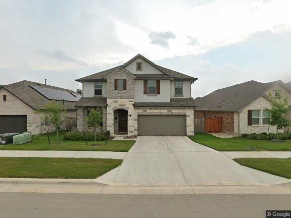 Two-story stone-and-siding home with an attached garage, wide driveway, and front lawn.