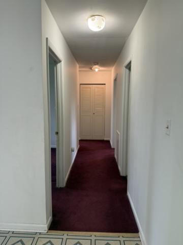 Hallway with burgundy carpet, white walls, and louvered closet doors at the far end.