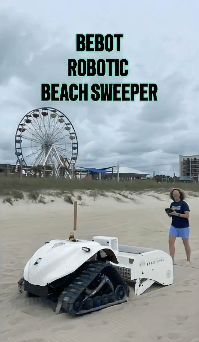 White Bebot robotic beach sweeper on the sand, with a woman and Ferris wheel behind it.