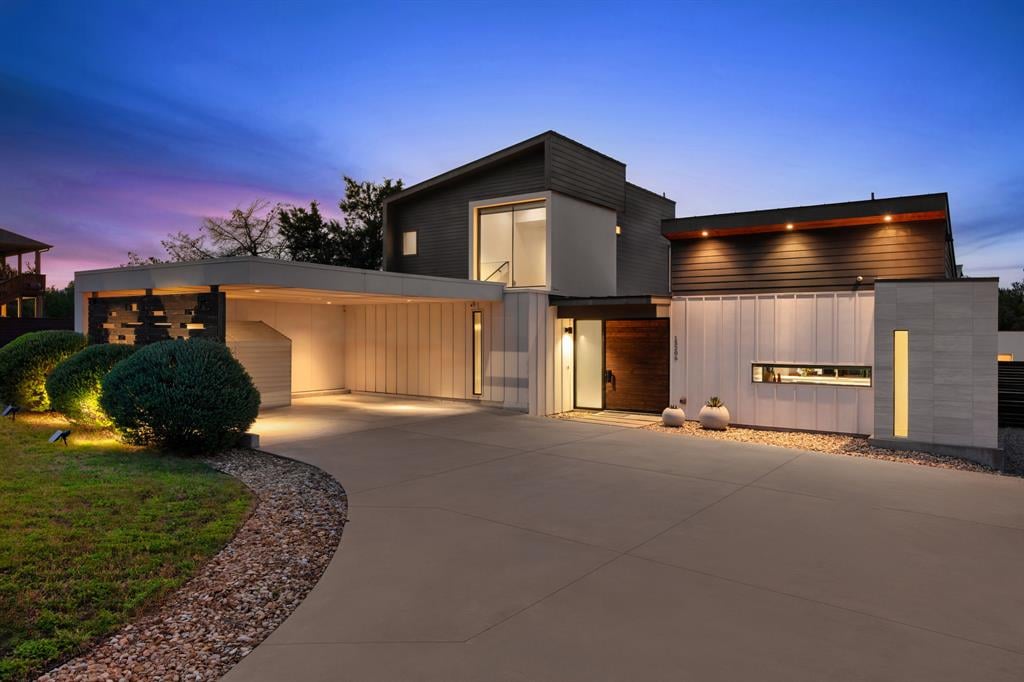 Modern home with geometric siding and a broad driveway, illuminated at dusk.