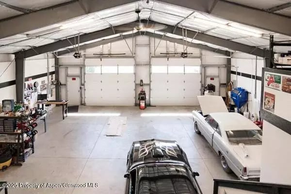 Large garage workshop with two overhead doors, workbenches, and two classic cars.