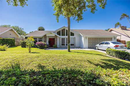 Single-story white home with a broad lawn, mature tree, and white car in the driveway.