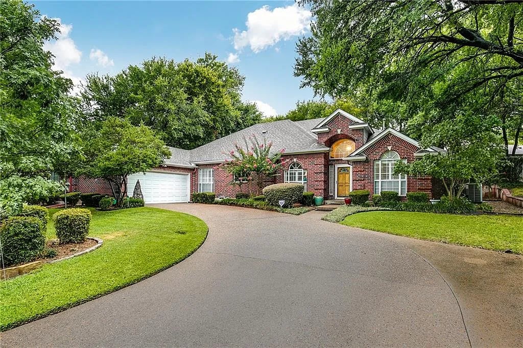 Red-brick house with an attached garage, curved driveway, and mature trees.