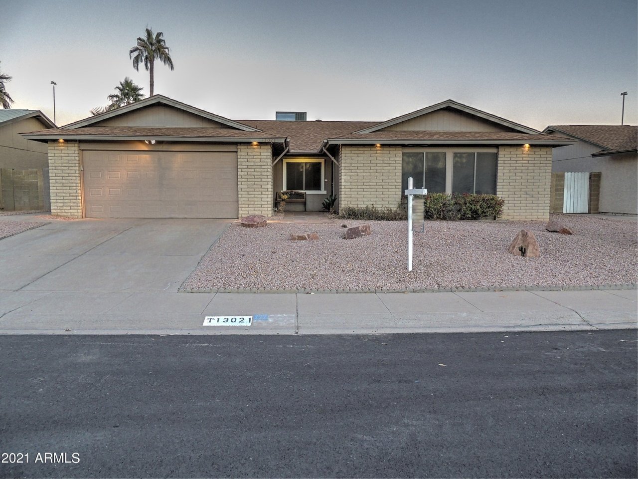 Single-story brick house with an attached garage, gravel landscaping, and a curb marked T 13021.