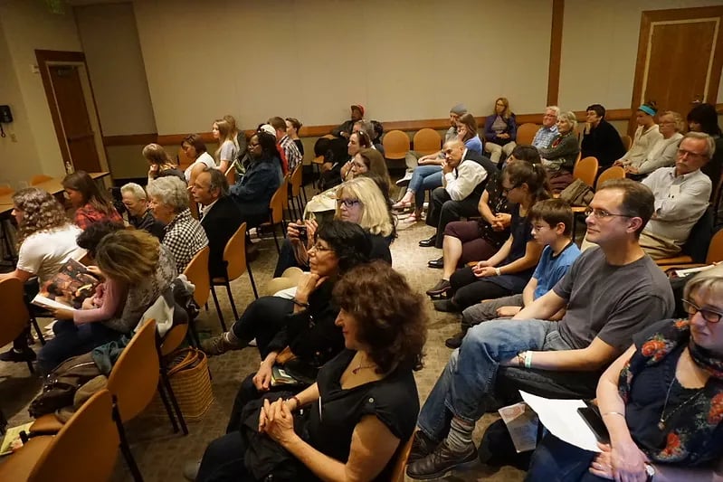 An attentive audience sits in rows of wooden chairs inside a lecture hall for the Bay Area Book Festival&rsquo;s Writers&rsquo; Competition. The diverse group of attendees, ranging from young students to seniors, is focused forward toward an unseen stage.