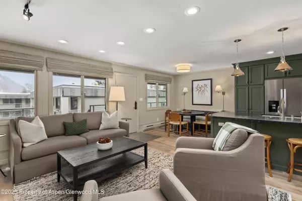 Open-plan living room and kitchen with gray sofas and deep green cabinetry.