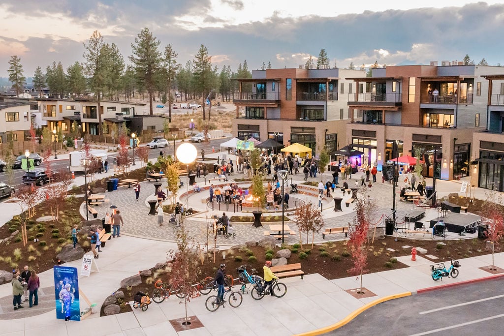 Discovery West neighborhood plaza with modern buildings, outdoor gathering, and cyclists at dusk.