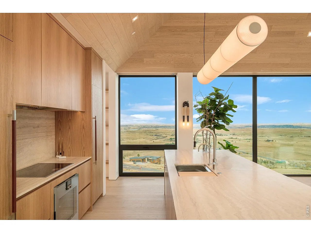 Modern wood kitchen with a large stone island and expansive landscape views through floor-to-ceiling windows.