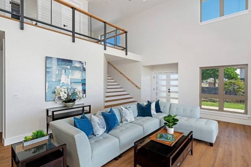 Living room with a pale sectional, blue pillows, wood floors, and an open staircase.