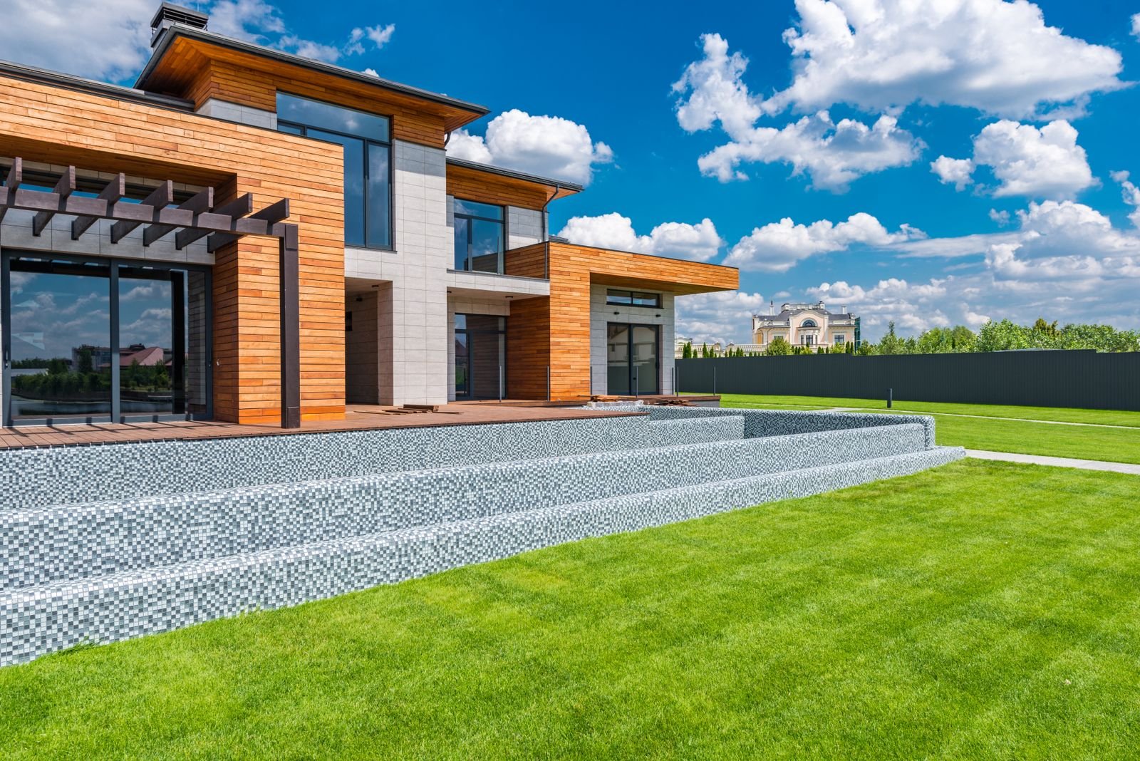 Contemporary house with a wood and stone exterior, large windows and a green lawn under a blue sky