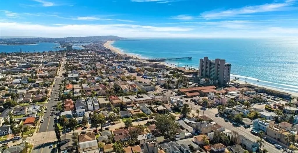 Aerial view looking south over Pacific Beach toward Mission Beach, featuring the iconic Crystal Pier, beautiful sandy beaches, Mission Bay, and the Pacific coastline at sunset in San Diego.