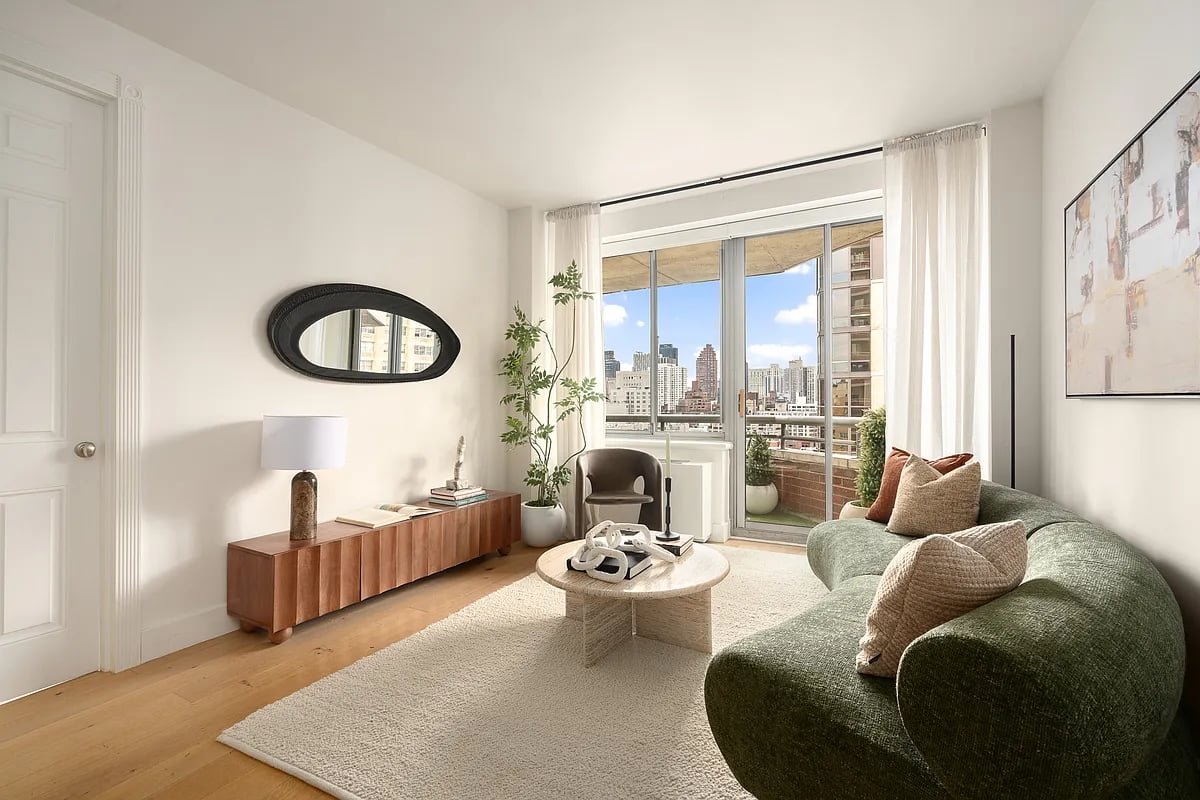 Bright living room with a green sofa and balcony doors overlooking the city skyline.