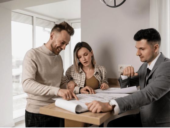 Three adults review architectural plans around a table in a bright room.
