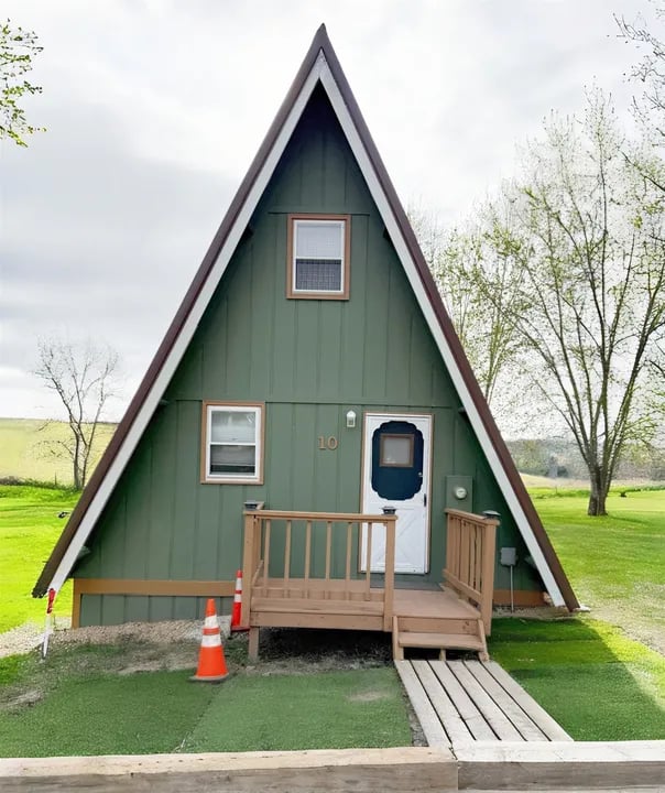 Green A-frame house with a raised wooden porch and plank walkway.