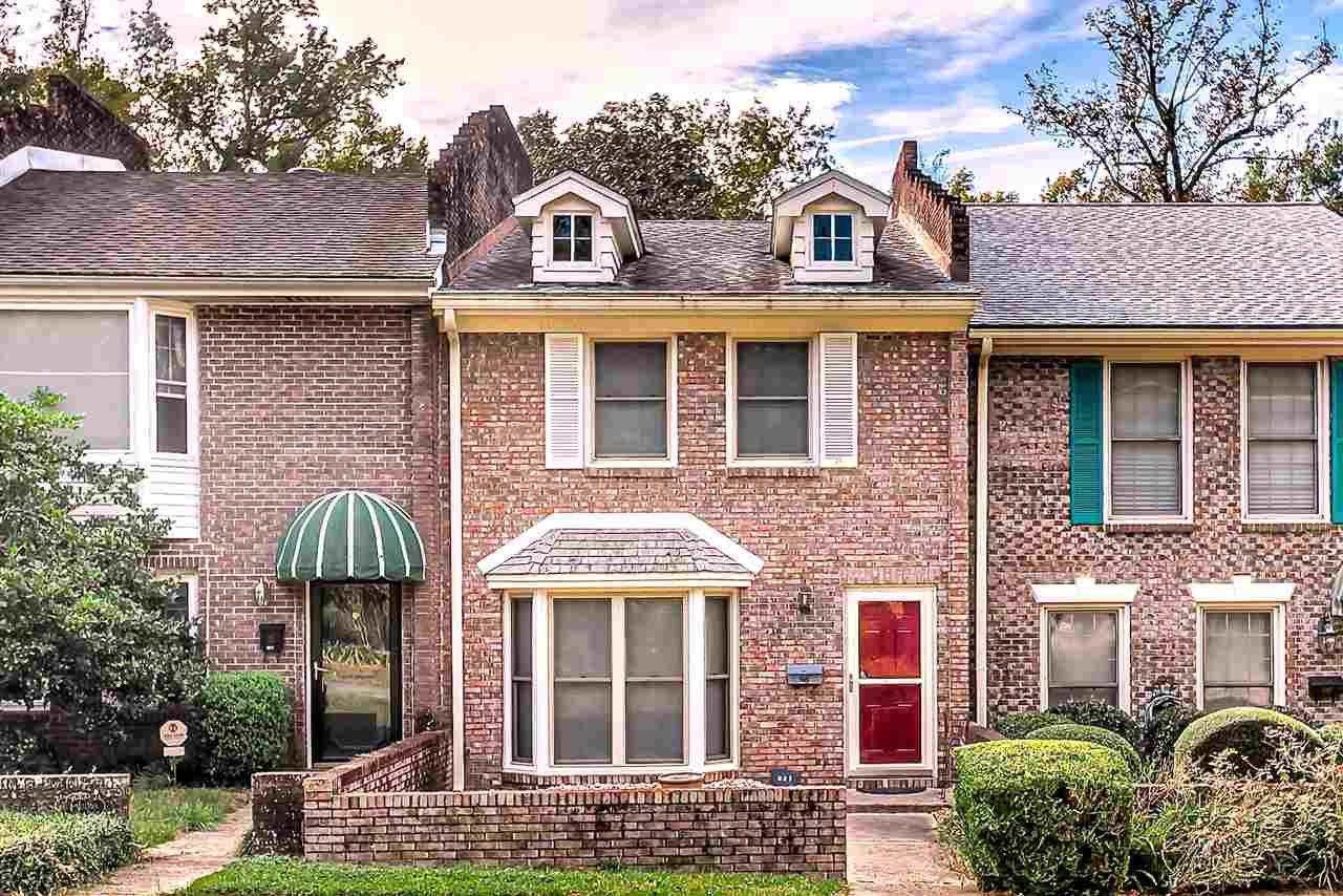 A brick townhouse featuring a vibrant red door and charming green shutters.