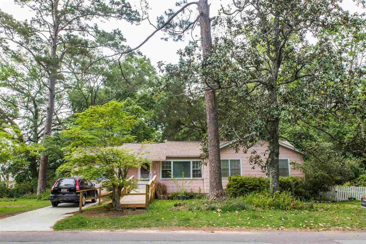 A small white house surrounded by a green lawn and trees, creating a serene and inviting outdoor environment.