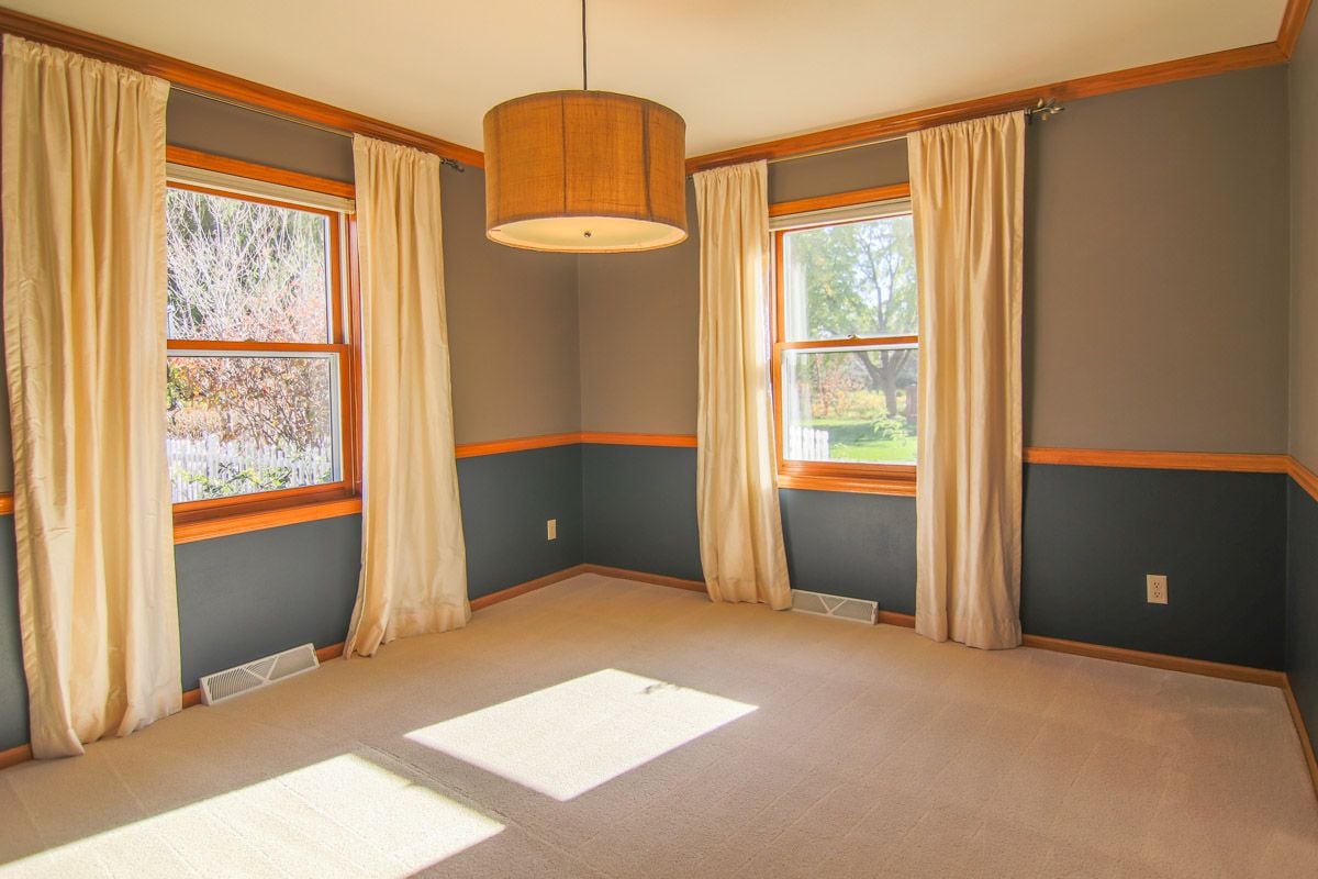 Vacant room with cream curtains, two windows, and a drum pendant light.