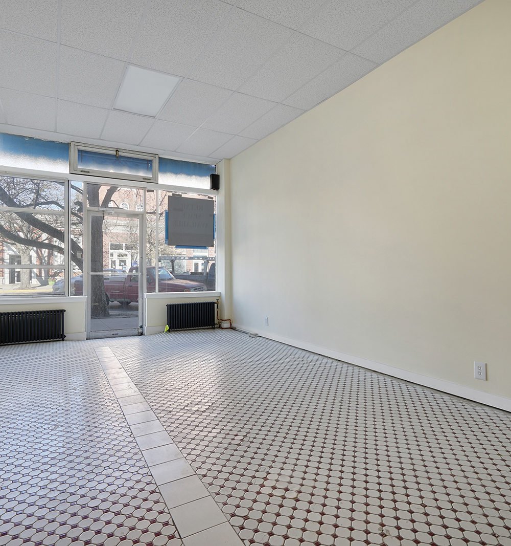 Vacant storefront with patterned tile flooring, large street-facing windows, and a glass entrance.