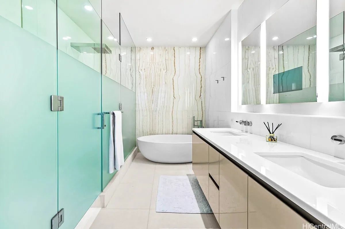 Modern bathroom with a glass shower, freestanding tub, veined stone wall, and double vanity.