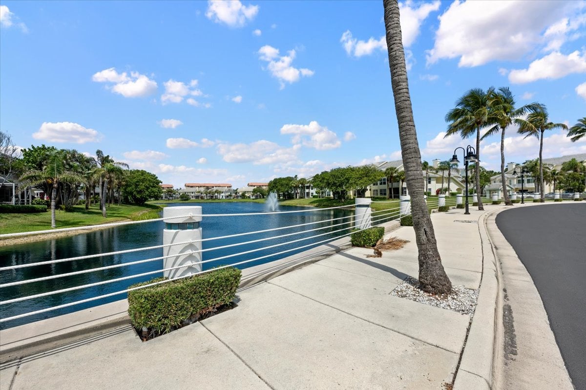 Sea Colony condominium residences beside a lagoon with a fountain, palm trees, and a curving sidewalk.
