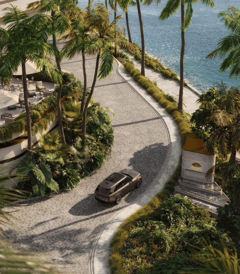 Waterfront condominium entrance with a curved cobblestone drive, tropical palms, and a luxury vehicle.