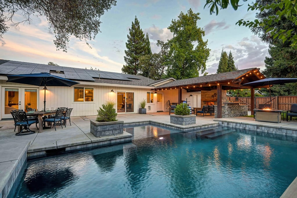 Backyard pool beside a single-story home with a covered outdoor kitchen and patio seating.