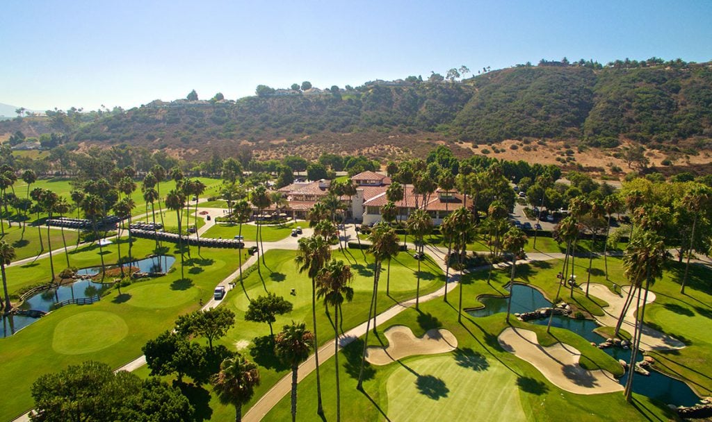 Aerial view of Fairbanks Ranch golf course and clubhouse surrounded by palm trees and hills, showcasing the luxury estate community in Rancho Santa Fe, San Diego.