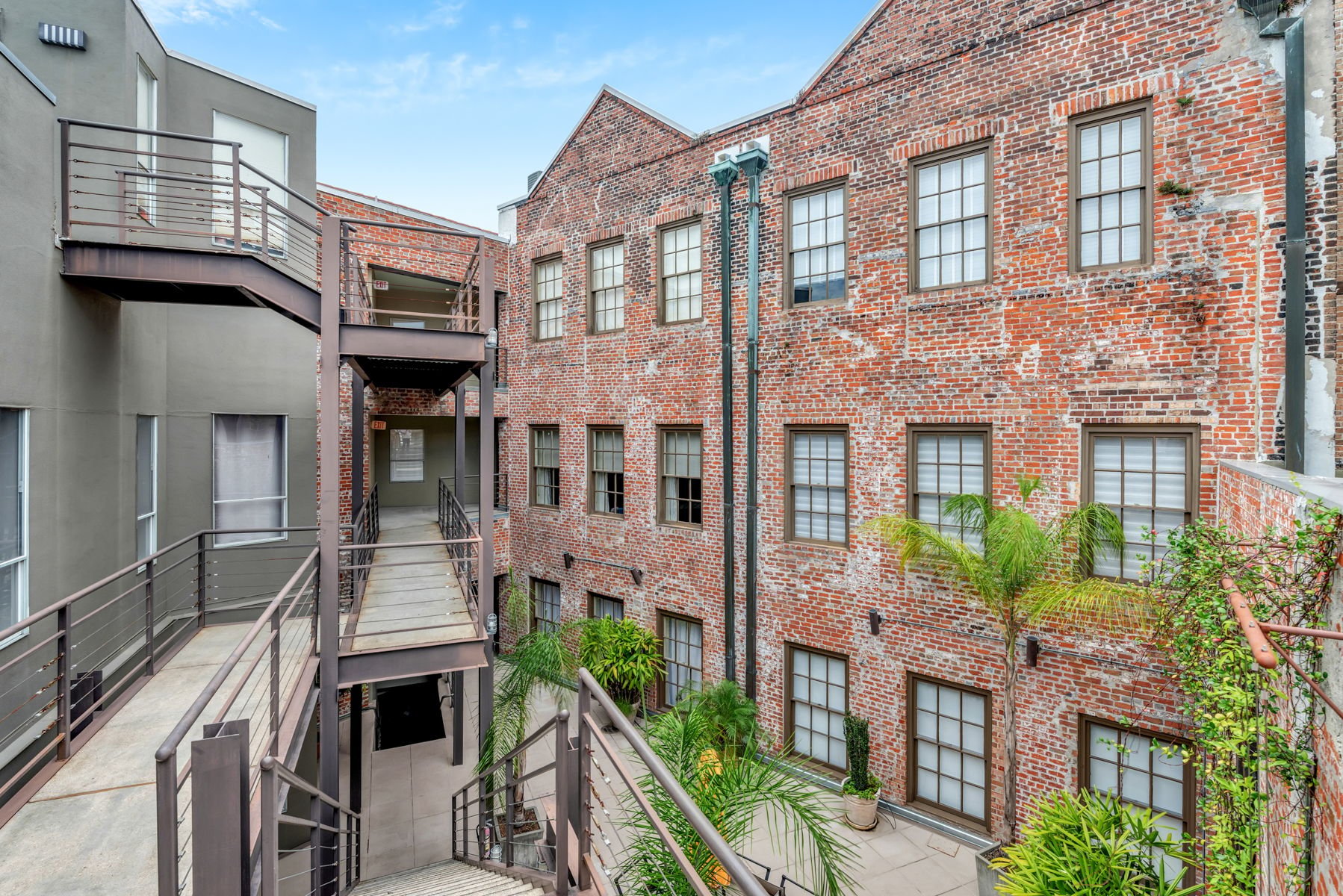 Brick loft courtyard with metal walkways and stairs, tall windows, and potted palms.