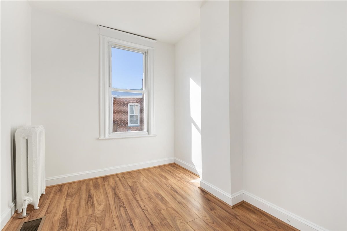 Empty room with warm wood flooring, a tall window, and a white radiator.