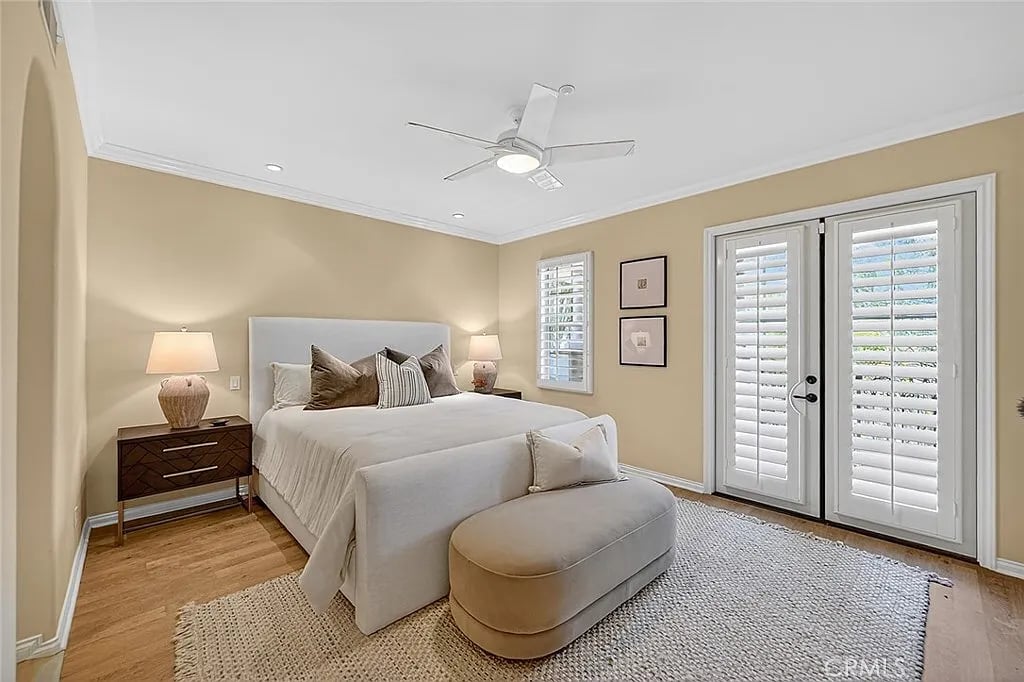 Staged bedroom with an upholstered bed, wood nightstands, plantation shutters, and a ceiling fan.