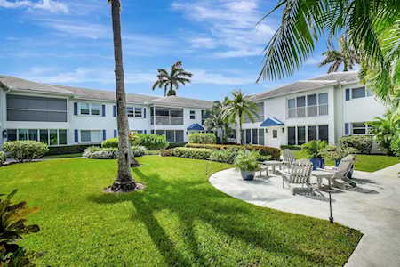 Condominium courtyard with a curved patio, outdoor seating, palm trees, and landscaped lawn.