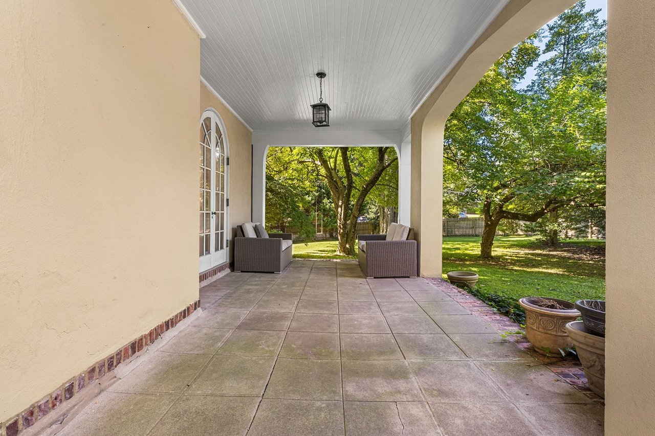 Covered patio with wicker seating, tiled floor, and leafy garden views.