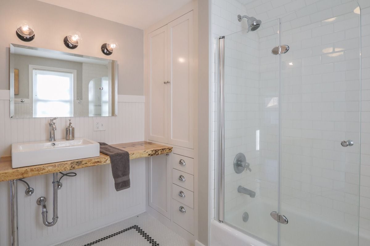 Bathroom with a natural-edge wood vanity and glass-enclosed subway-tile shower.