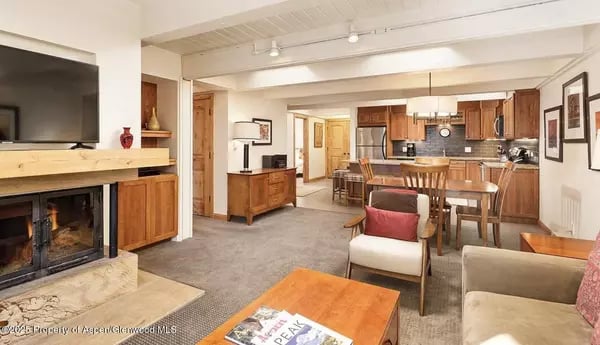 Open-plan living and dining area with a stone fireplace, wood cabinetry, and adjoining kitchen.