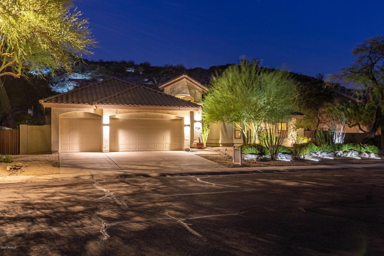Desert-style home at night with a lit two-car garage and desert landscaping.