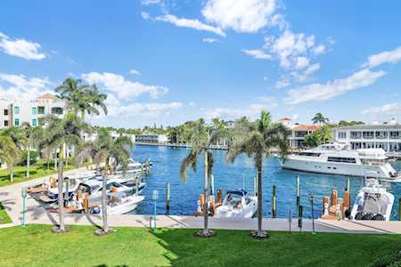 Waterfront marina with docked boats, palm trees, and low-rise buildings along a blue canal.