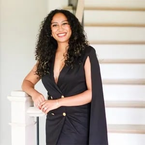 Kathleen Patterson smiling beside a white staircase in a black cape-style outfit.