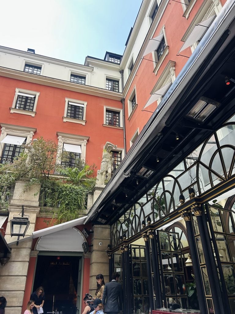 Red courtyard façade with ornate windows and a black-and-gold arched glass storefront.