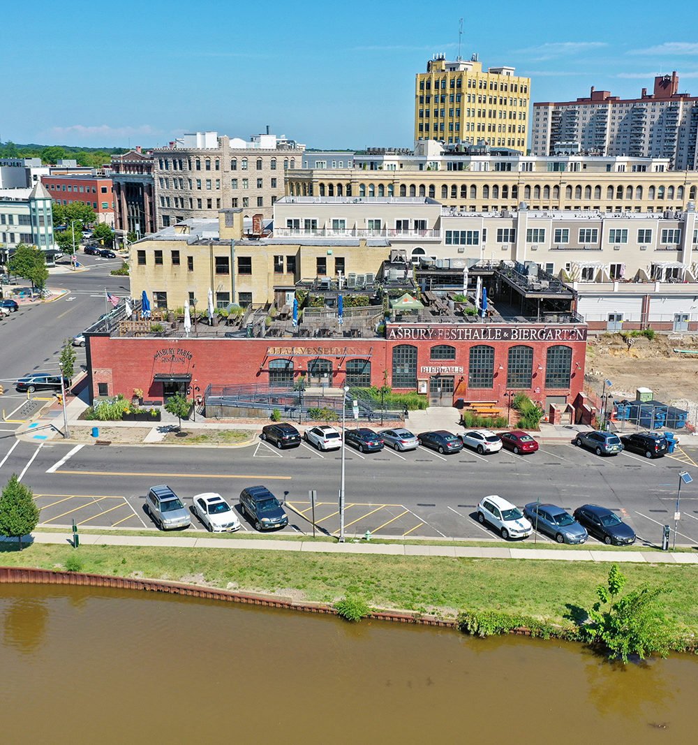 Aerial view of a red-brick commercial building with rooftop terraces beside a waterway.